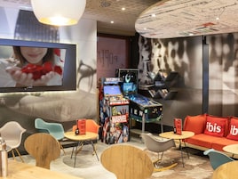Un'area lounge moderna con schermo piatto, macchinette da gioco, posti a sedere confortevoli e una parete decorata con un grande poster.