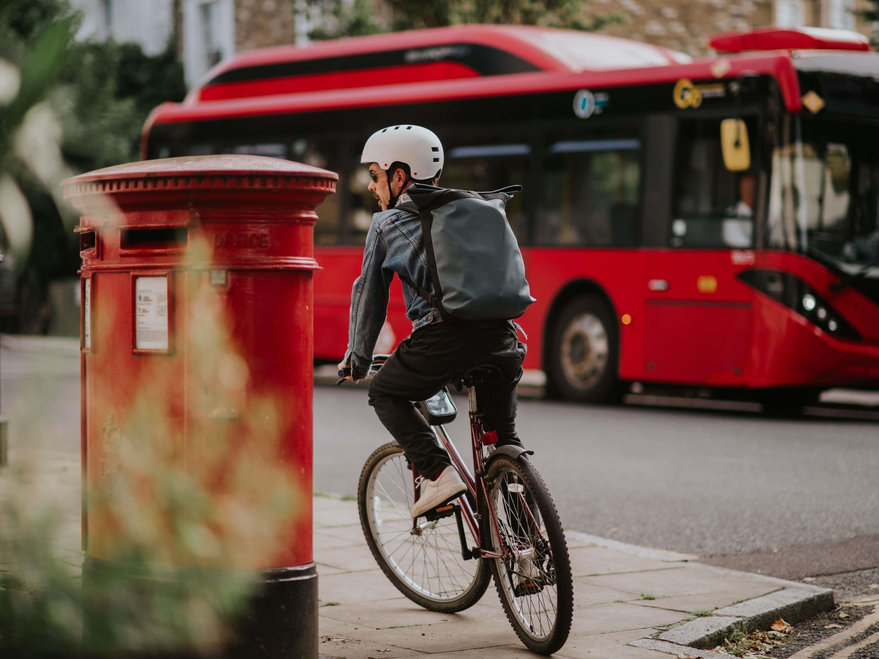 A person riding a bicycle on a sidewalk, a red mailbox, and a red bus in the background.