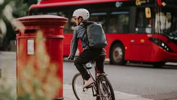 A person riding a bicycle on a sidewalk, a red mailbox, and a red bus in the background.