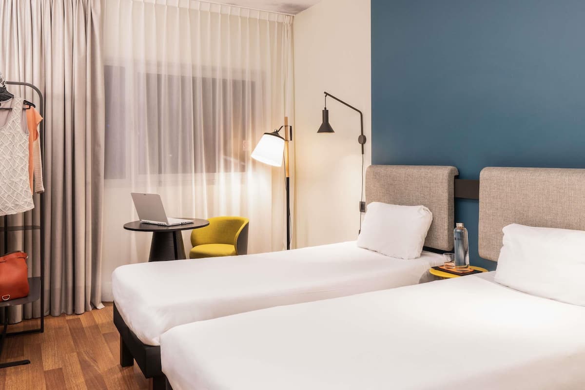 A hotel room with two beds, a desk with a laptop, a chair, a lamp, and a wardrobe.