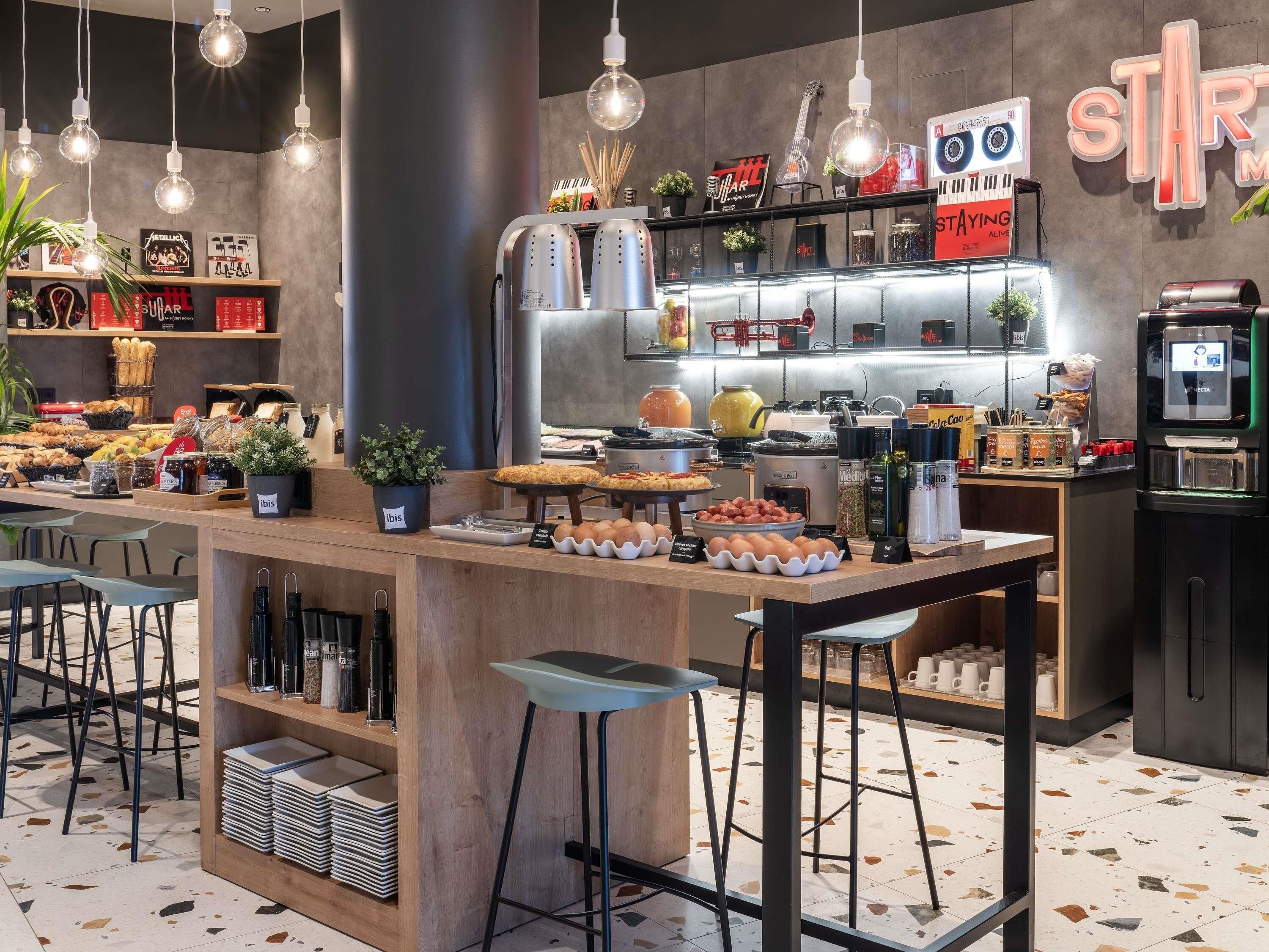 Een café met een toonbank waarop gebak, een koffiemachine en een bord met de tekst 'STAYING ALIVE' staan.