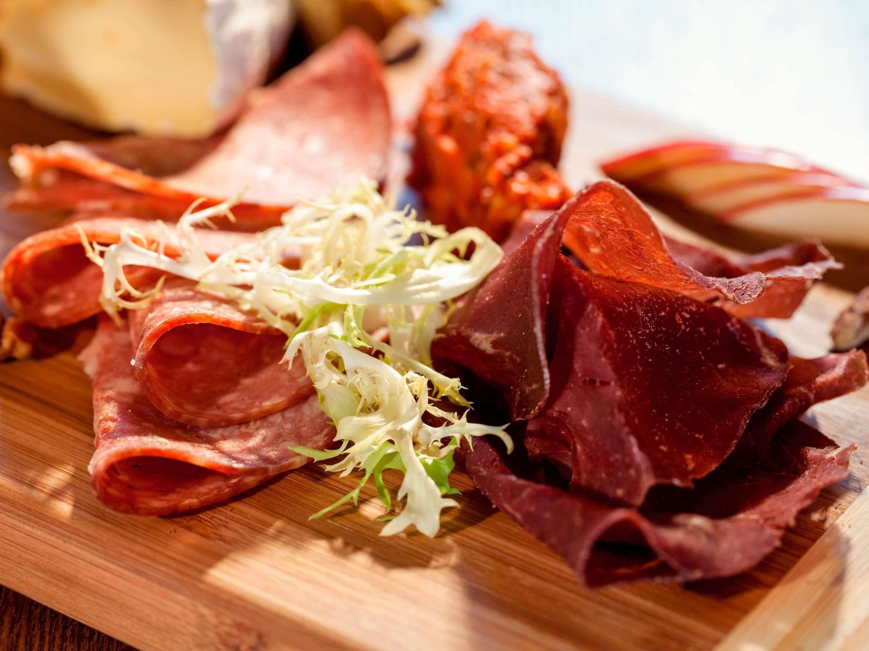 Une planche à découper en bois, sur laquelle on a disposé différentes sortes de charcuterie et de la laitue émincée.