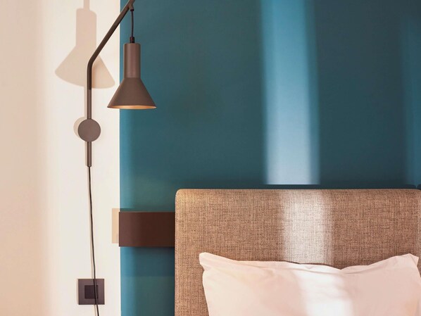 A modern bedroom with a textured headboard, a single white pillow, and a wall-mounted lamp.