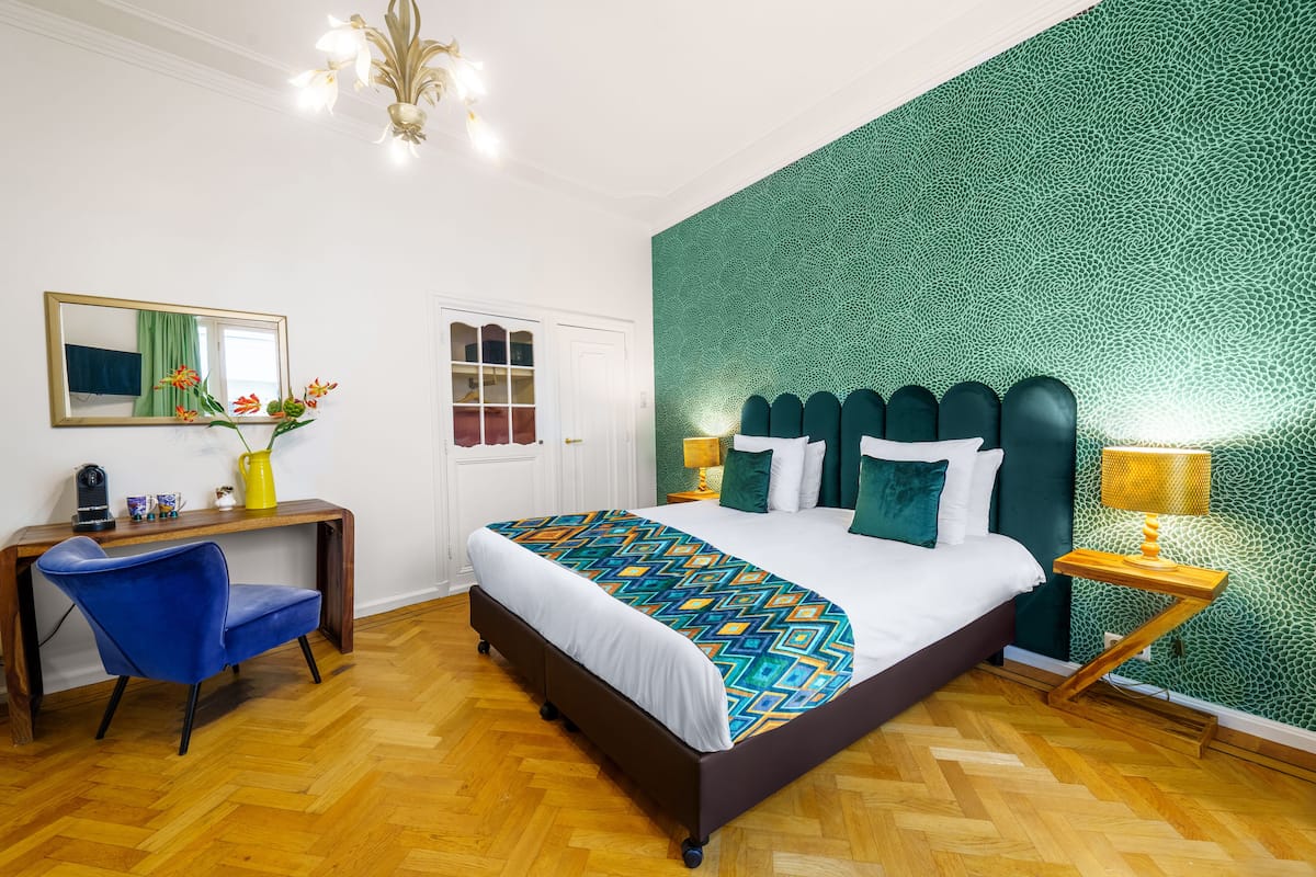 A bedroom with a bed, a desk with a chair, a mirror, and a green textured wall.