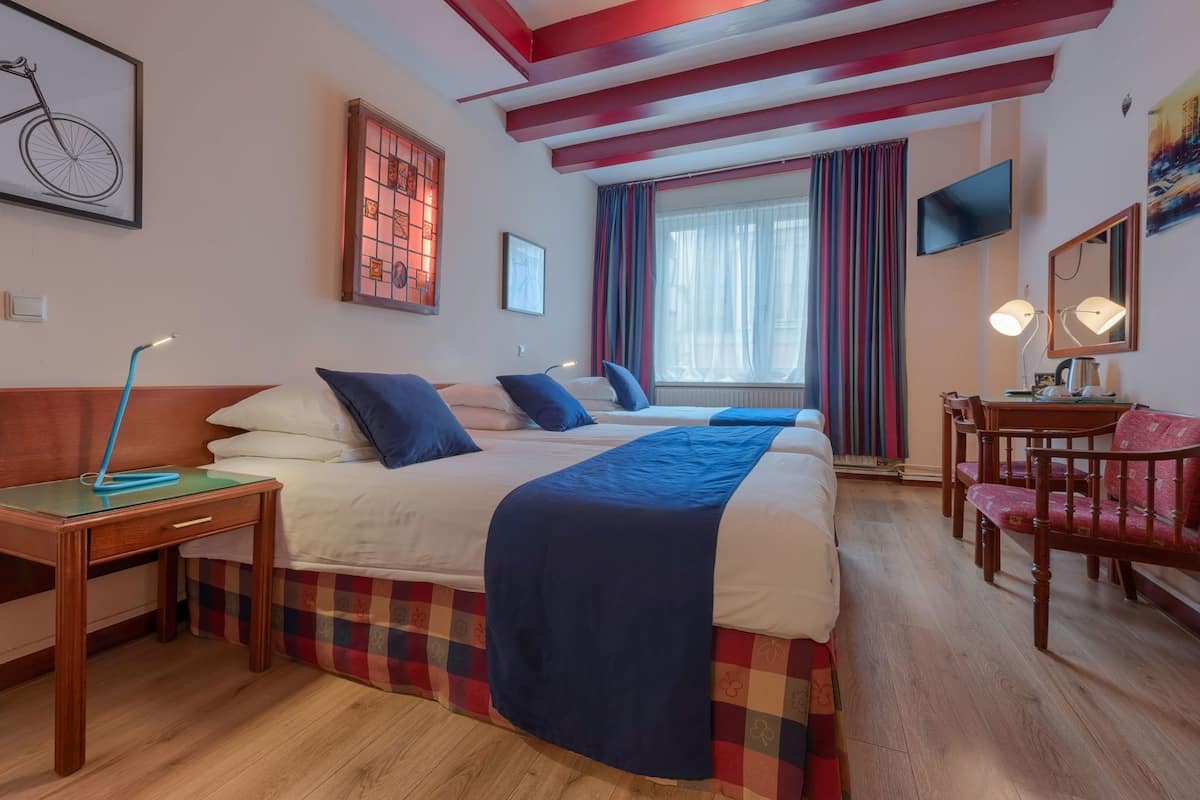 A hotel room with a bed, a desk, a chair, a television, and a window with curtains.
