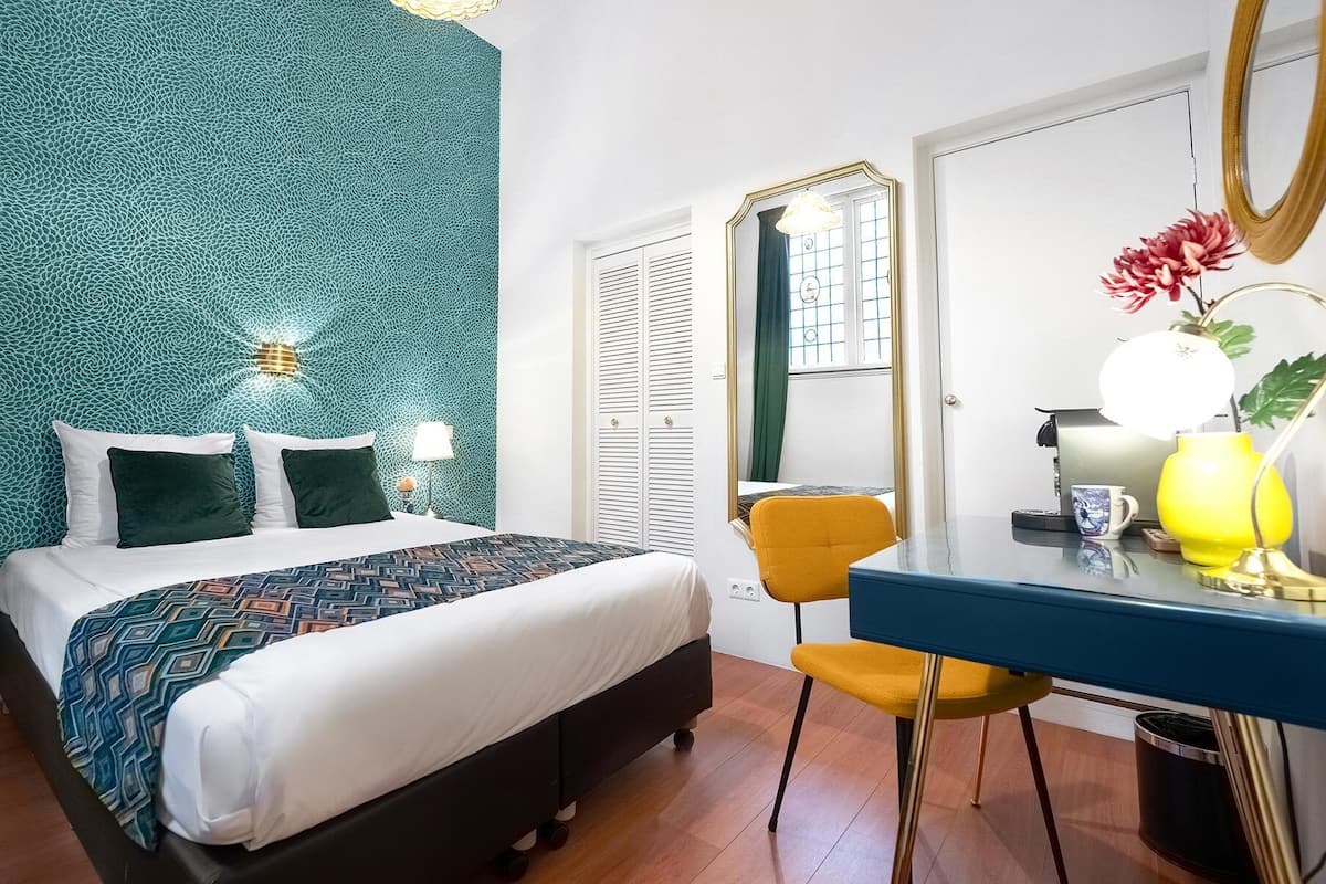 A hotel room with a bed, a desk, a chair, and a mirror.