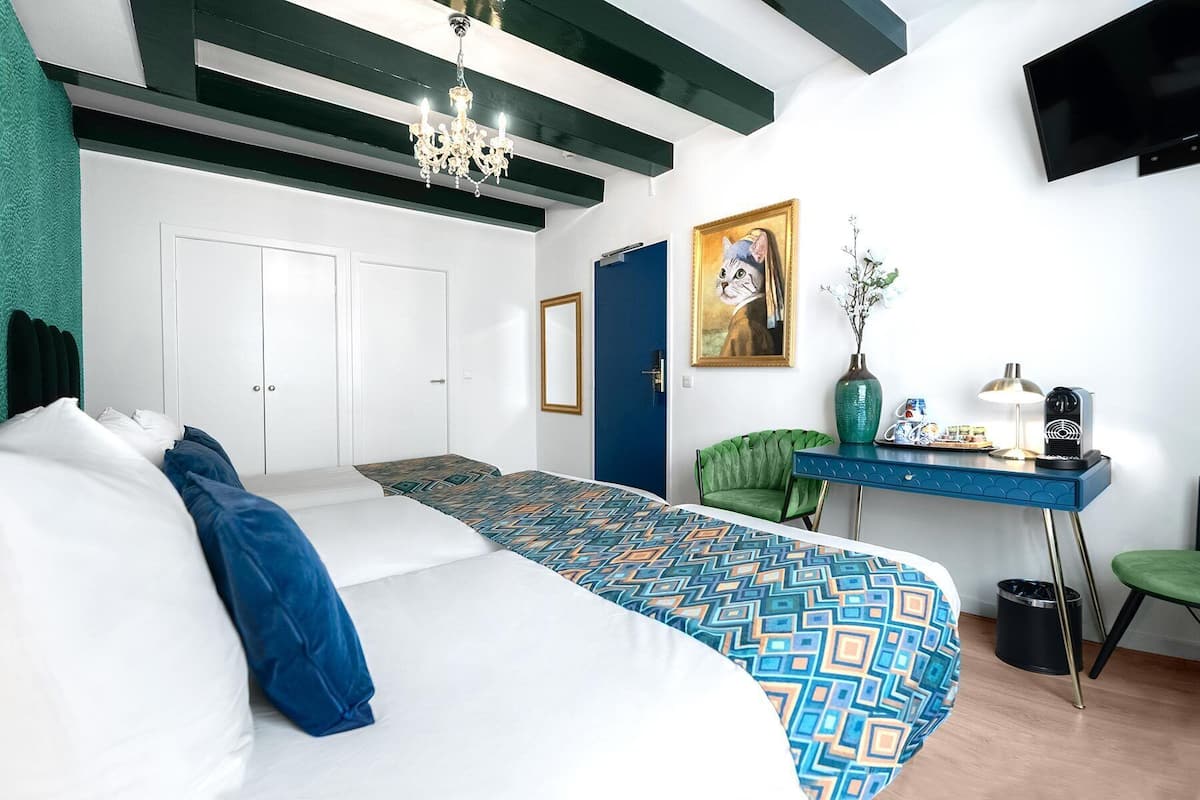 A modern hotel room with a large bed, a desk with a chair, a painting, and a TV on the wall.