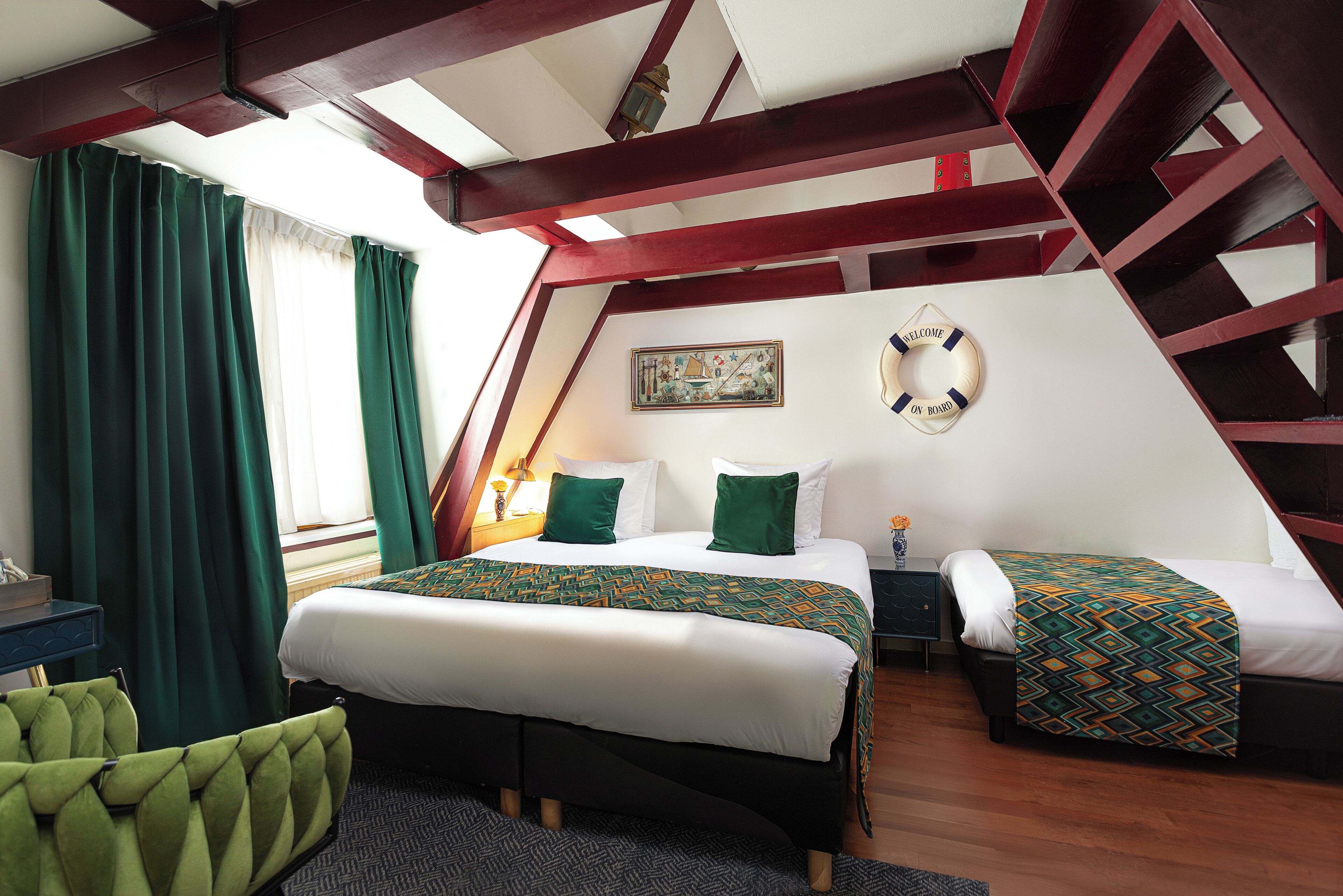 A bedroom with two beds, a green chair, a painting, and a welcome sign.
