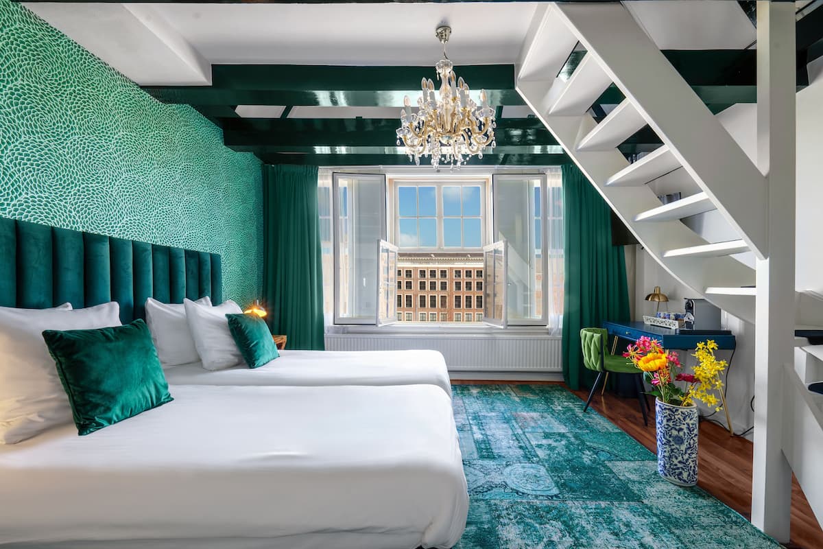 A modern hotel room with a large bed, a desk, and a view of the city through a window.