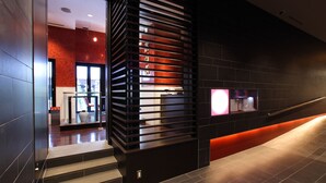 A modern lobby with a staircase leading to an upper level, a reception desk, and a wall-mounted television. - Hotel Monterey Hanzomon (Tokyo)