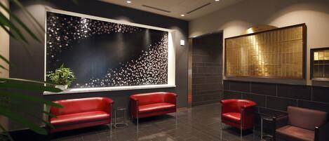 A modern lobby with dark tiled flooring, red leather seating, a large abstract wall art, and a traditional Japanese screen.
