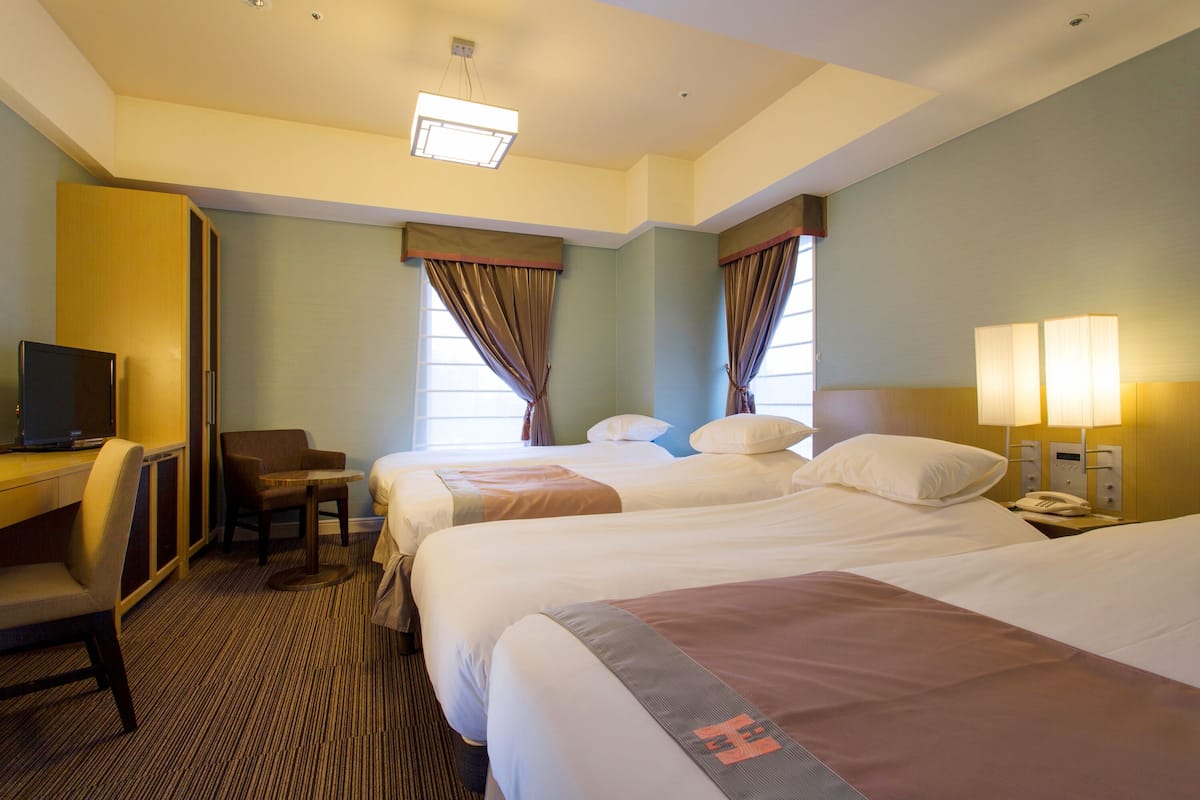 A hotel room with two beds, a desk with a chair, a TV, and a lamp.