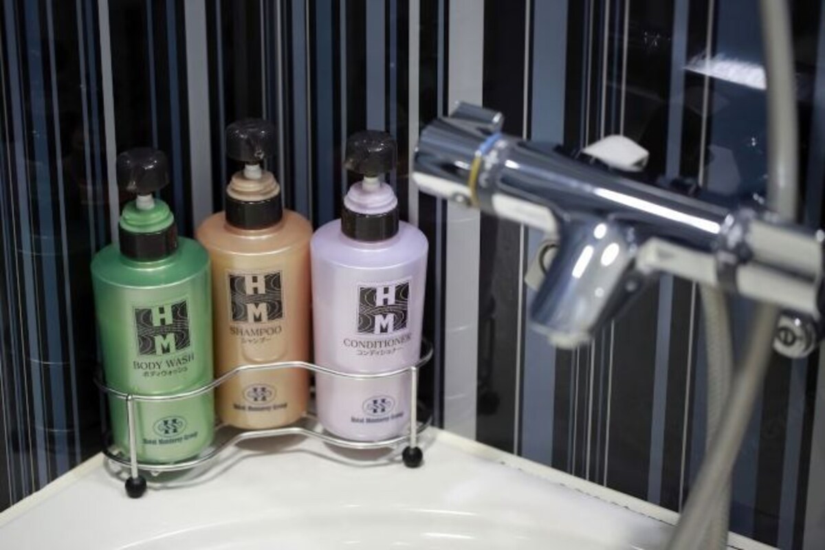 Ett badrum med ett handfat, en spegel och tre flaskor med H&M:s duschkräm, schampo och balsam på en hylla.