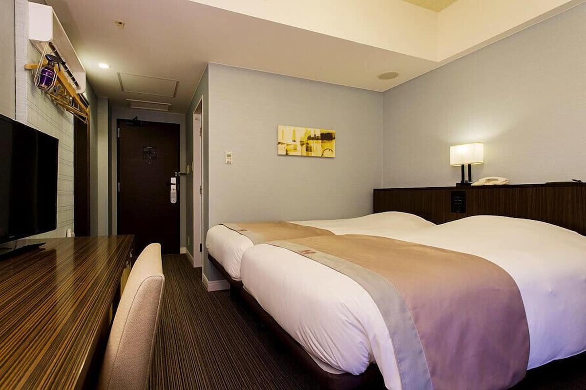 A hotel room with a bed, a desk, a chair, a TV, and a painting on the wall.