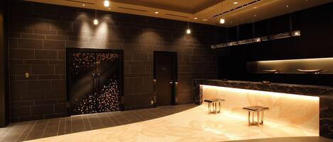 A modern hotel lobby with a curved reception desk, dark tiled walls, and a patterned floor.