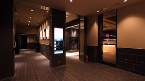 A modern hotel corridor with a digital information kiosk, a fire extinguisher, and a reception area with a counter. - Hotel Monterey Hanzomon (Tokyo)
