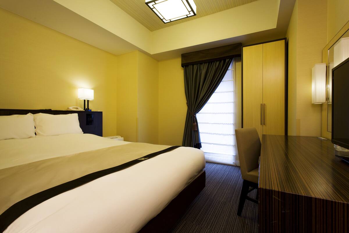 A hotel room with a large bed, a desk, a chair, a television, and a window with curtains.