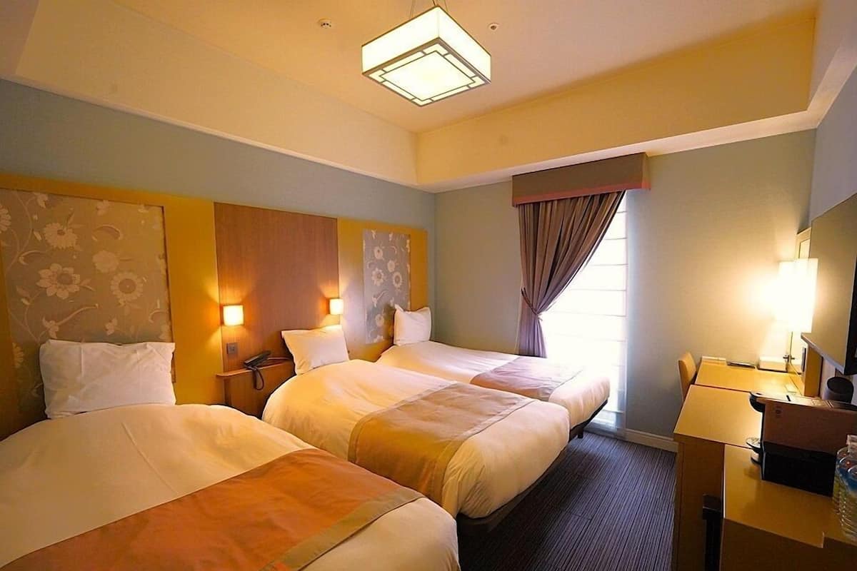 A hotel room with two beds, a desk, a chair, and a window with curtains.
