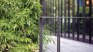 A wooden deck with a metal railing and a bamboo plant. - Hotel Monterey Hanzomon (Tokyo)