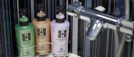 Baño con lavamanos, espejo y tres botellas de gel de baño, champú y acondicionador H&M sobre una estantería.