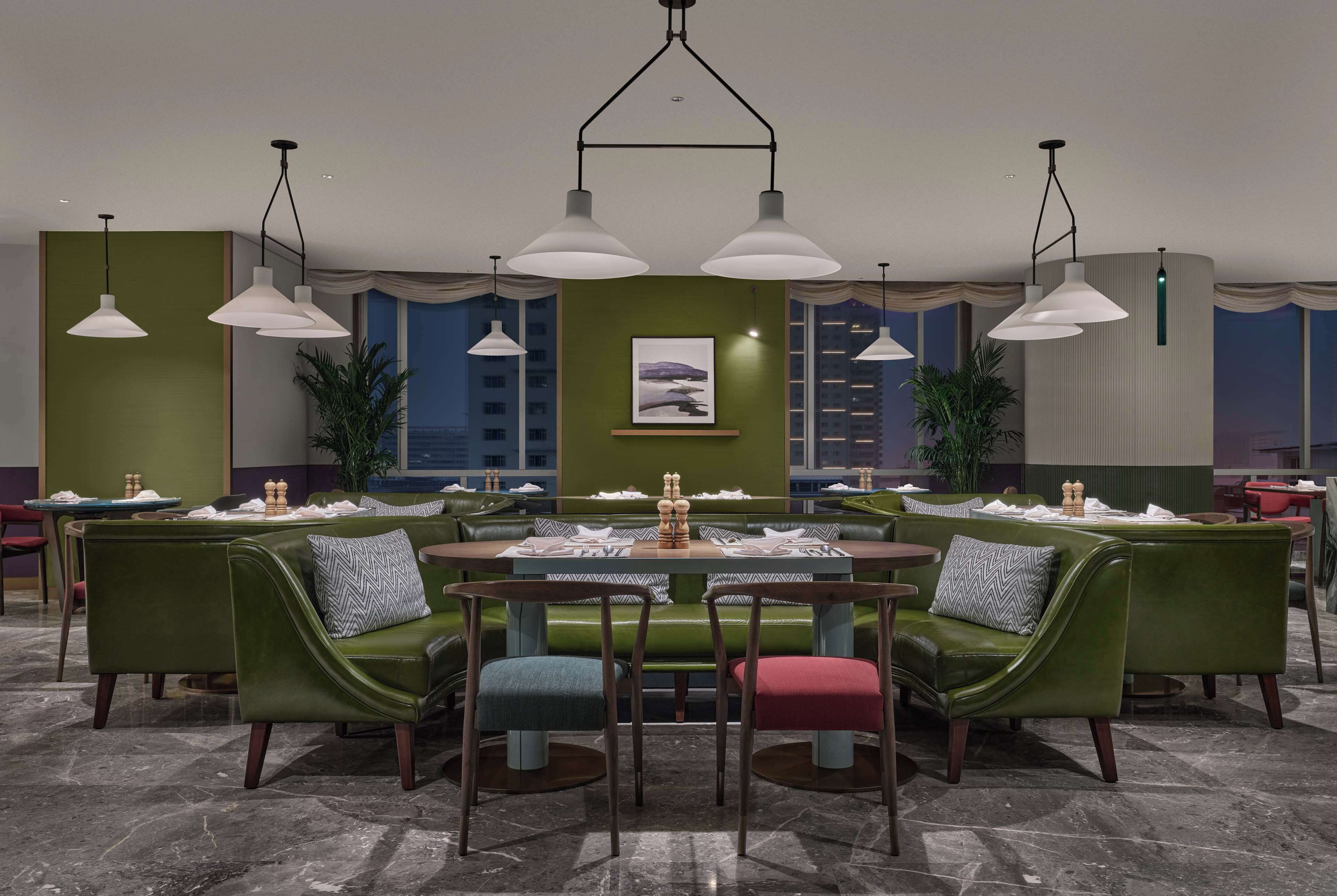 A modern dining area with green upholstered booths, a round table, and pendant lighting.