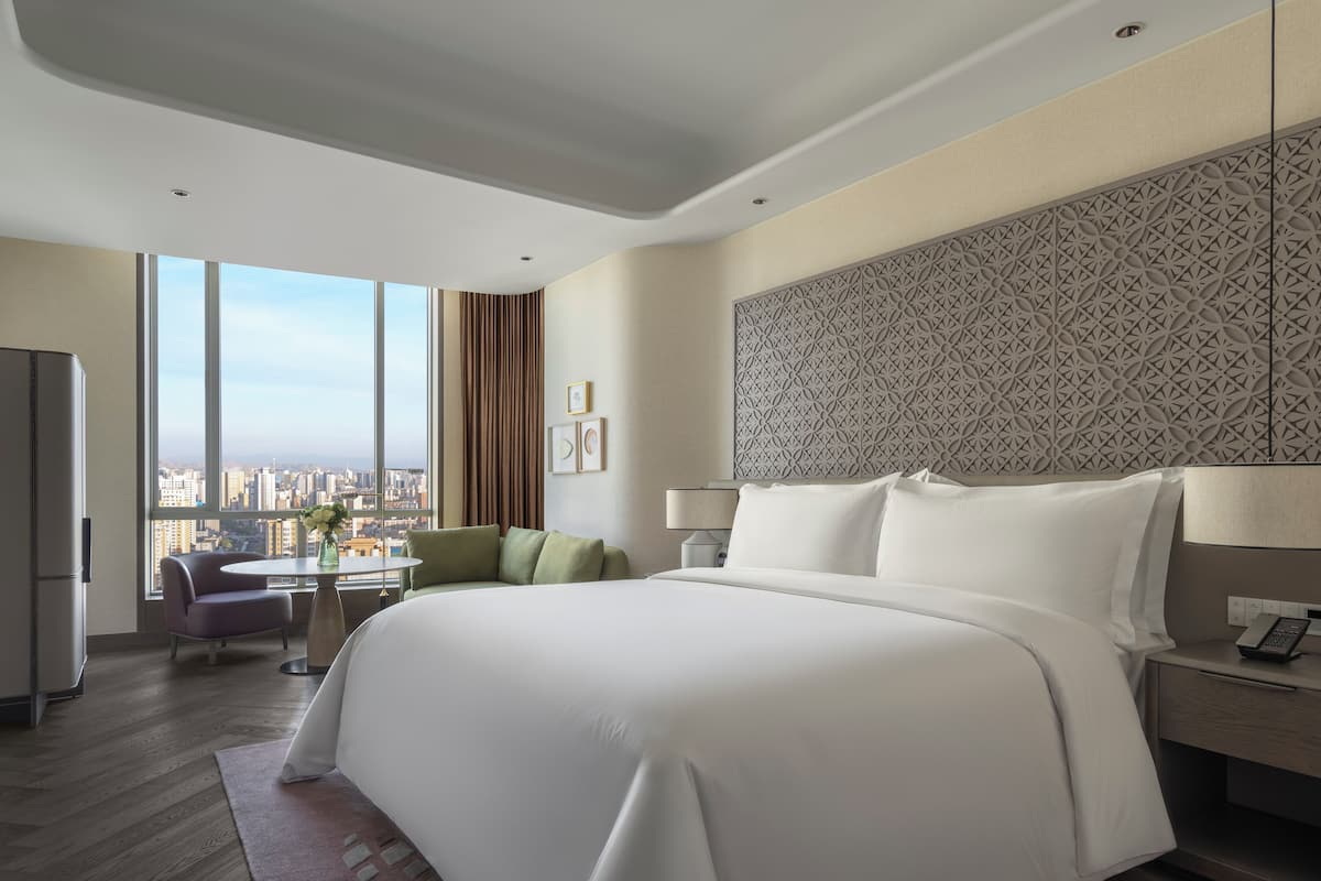 A modern hotel room with a large bed, a desk, and a view of the city.