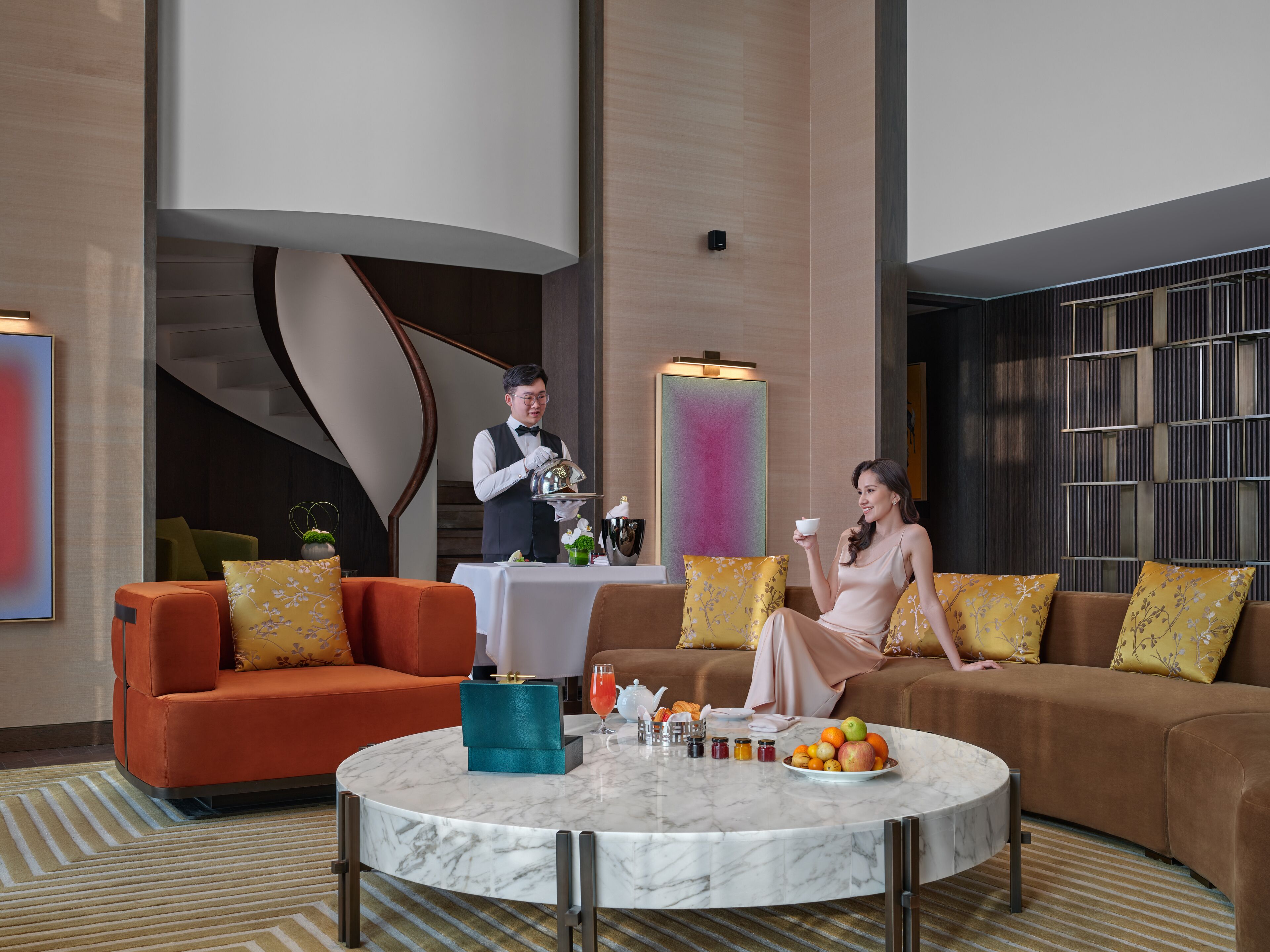 Un moderno vestíbulo de hotel con una mesa de café de mármol, sofás naranja y marrón, y un cuadro abstracto grande en la pared.