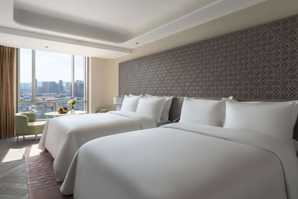 A hotel room with two large beds, a city view, a patterned headboard, and a small table with a vase of flowers.