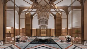 A spacious lobby with a geometric ceiling design, a central water feature, and seating areas.