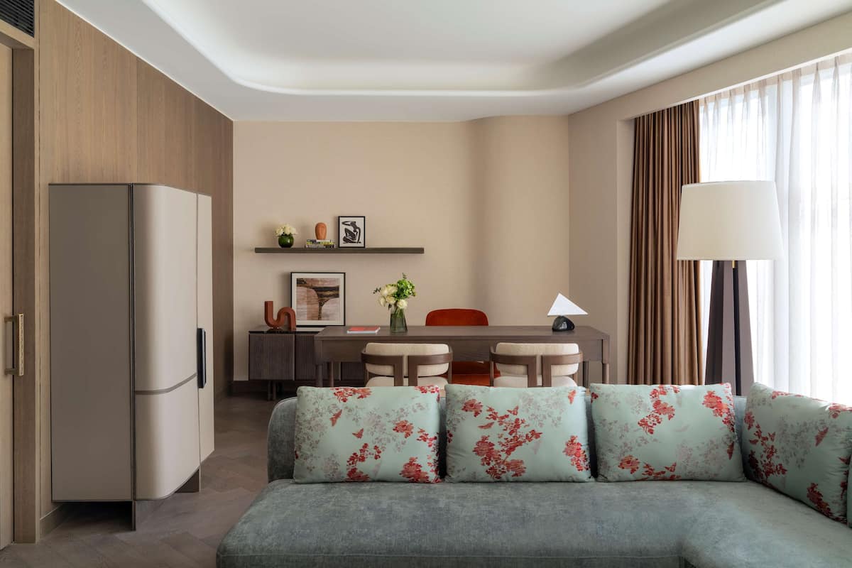 A modern hotel room with a kitchenette, a dining area, and a sofa with floral cushions.