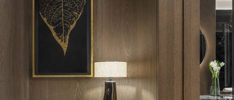 A wooden panel wall with a framed artwork, a marble-topped table with a lamp, and a vase with flowers.