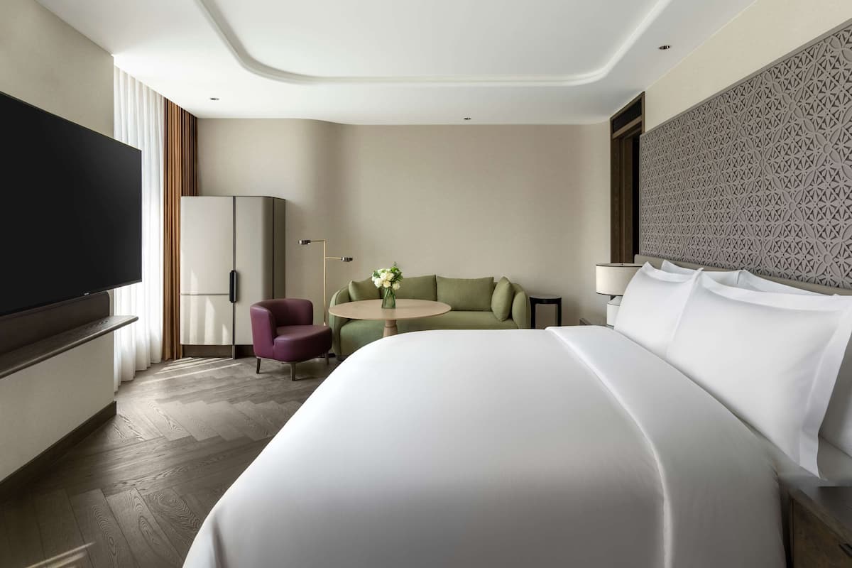 A hotel room with a large bed, a flat-screen TV, a sofa, a small table, and a decorative wall panel.