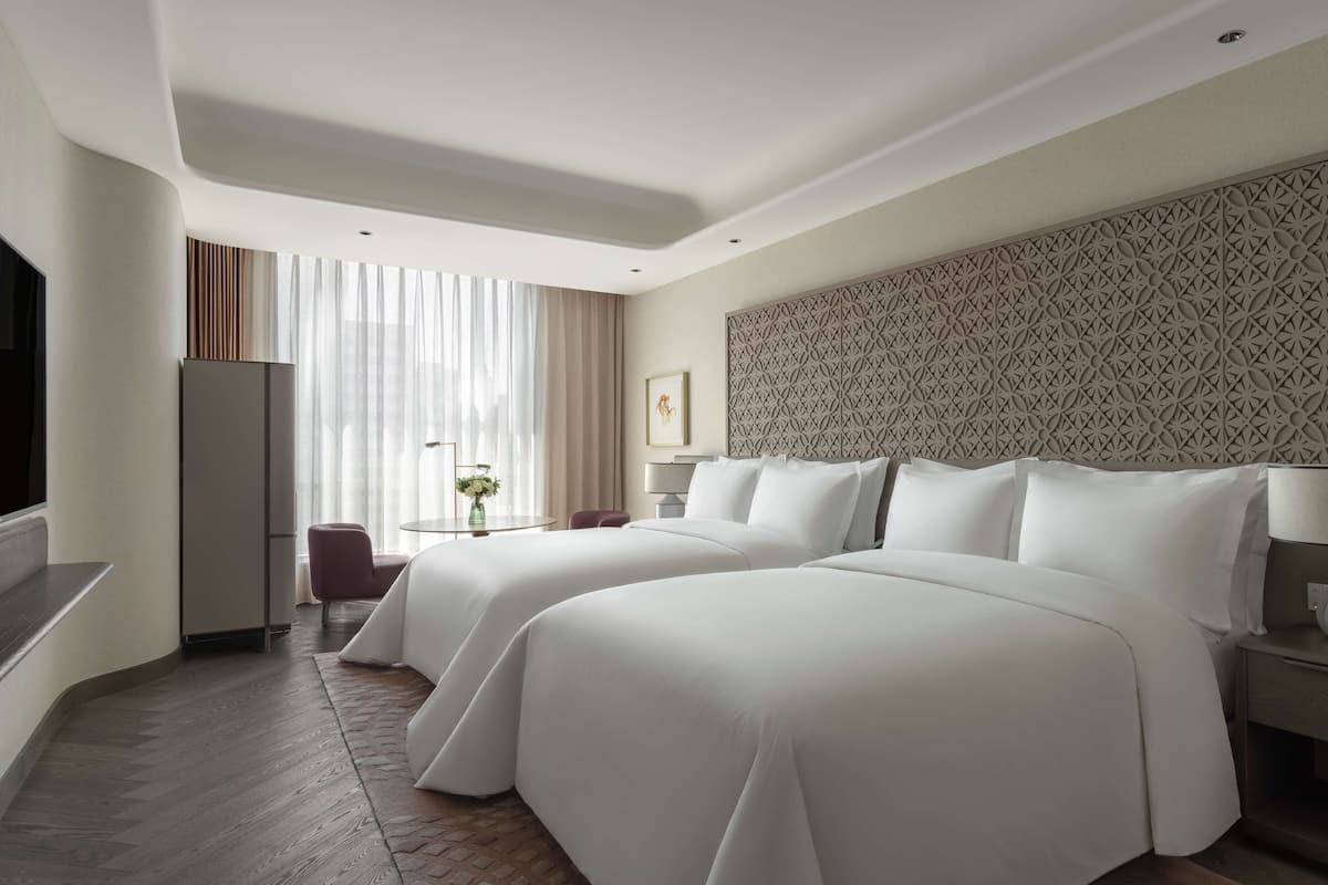 A hotel room with two beds, a TV, a desk, and a patterned headboard.