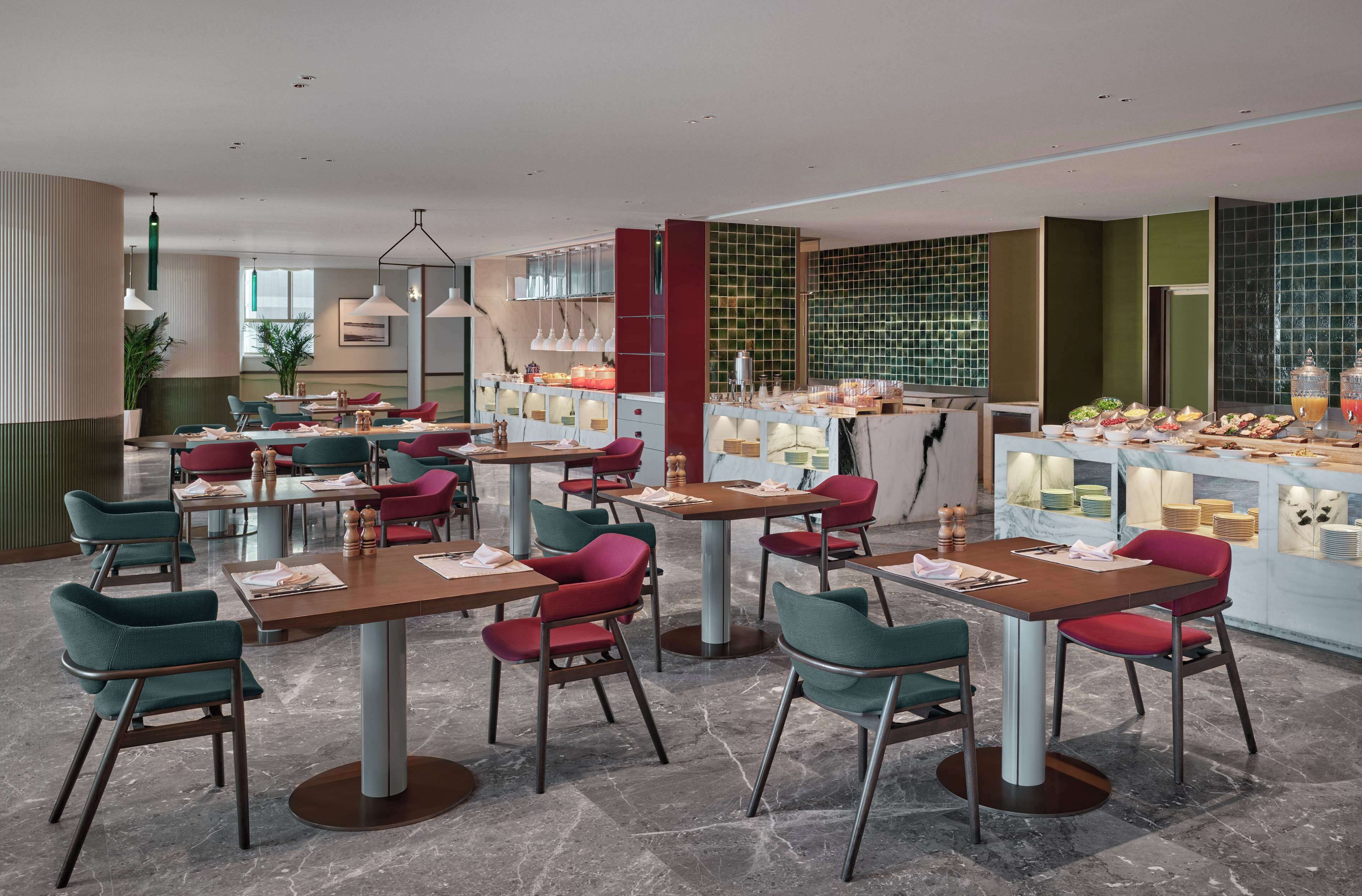 Um restaurante moderno com várias mesas e cadeiras, um balcão com expositores de comida e um design de interiores limpo e contemporâneo.