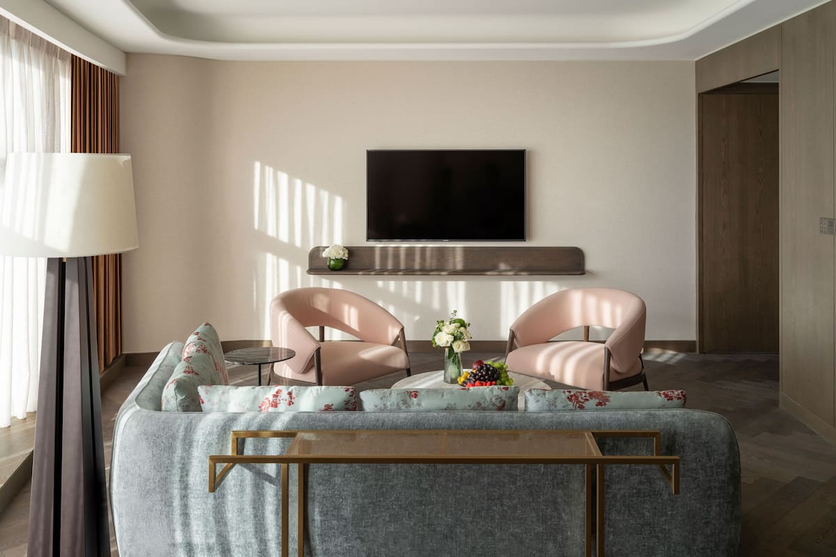 A modern living room with a sofa, two armchairs, a coffee table, a flat-screen TV mounted on the wall, and a small side table with a vase of flowers.