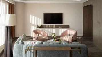 Una sala de estar moderna con un sofá, dos sillones, una mesa de centro, un televisor de pantalla plana montado en la pared y una mesita auxiliar con un jarrón de flores.