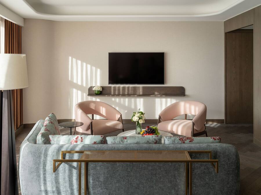 Una sala de estar moderna con un sofá, dos sillones, una mesa de centro, un televisor de pantalla plana montado en la pared y una mesita auxiliar con un jarrón de flores.