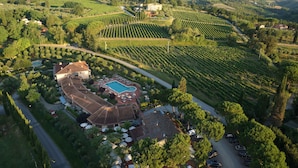 Vista aérea de una finca vitivinícola con campos en terrazas, una piscina y un edificio curvo con techo de tejas.
