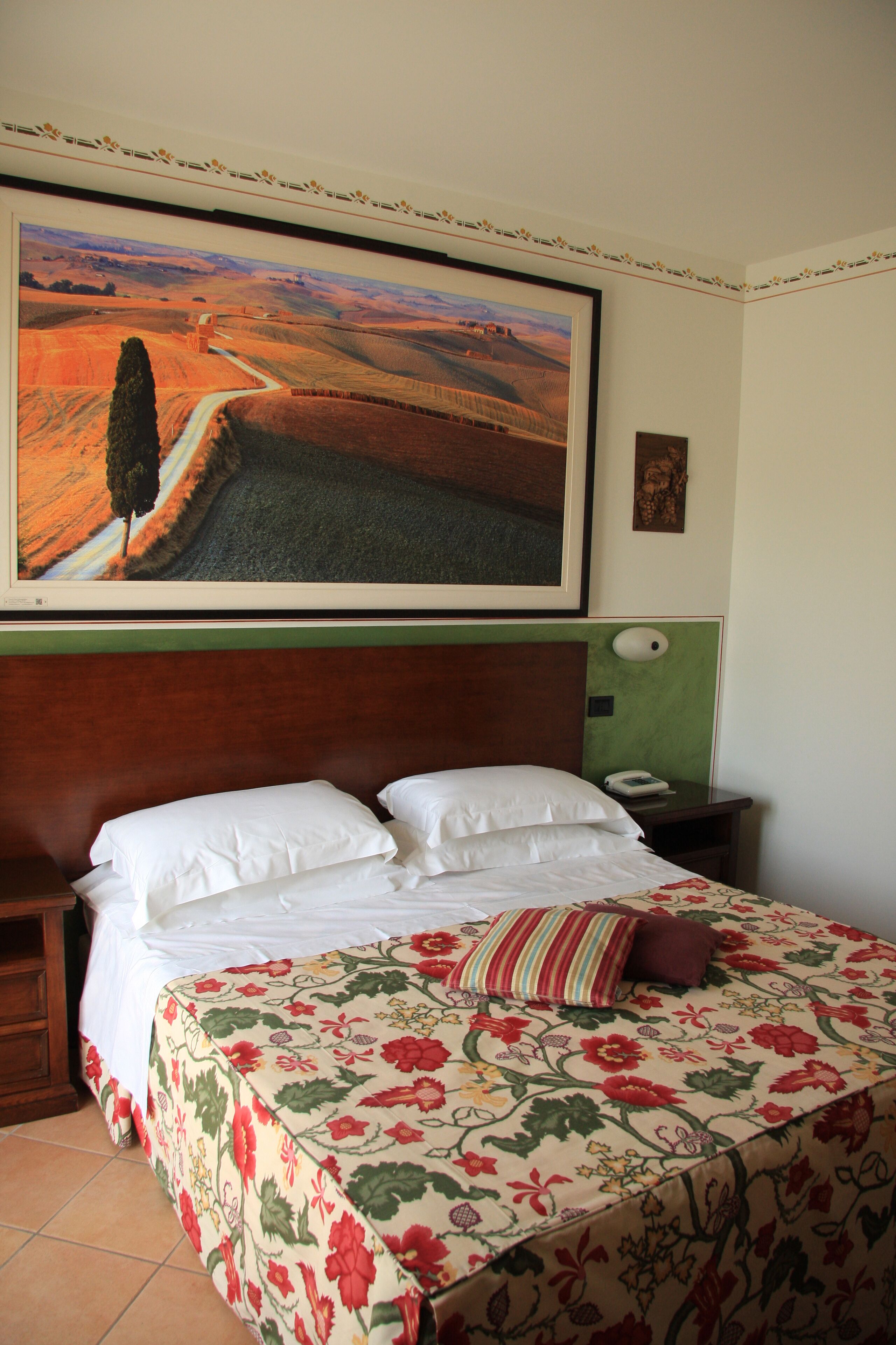 A hotel room with a large bed, a nightstand, a telephone, and a painting of a landscape.