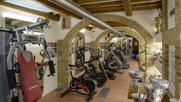 A gym with exercise equipment, a red bench, and a table with trophies.