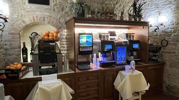 Un café con paredes de piedra, una máquina de café, una botella de vino y naranjas sobre la barra.