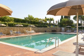 Una piscina con tumbonas y sombrillas, rodeada de muros de piedra y vegetación.