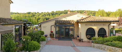 A hotel named "Hotel Sovestro" with a tiled roof, a covered entrance, and a garden area with potted plants and a pathway.