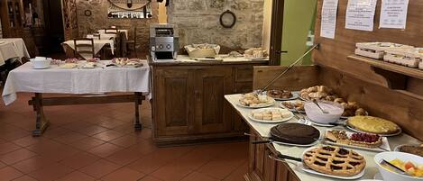 Zona de bufé con diferentes alimentos, una máquina de café y una pared de piedra con un reloj.