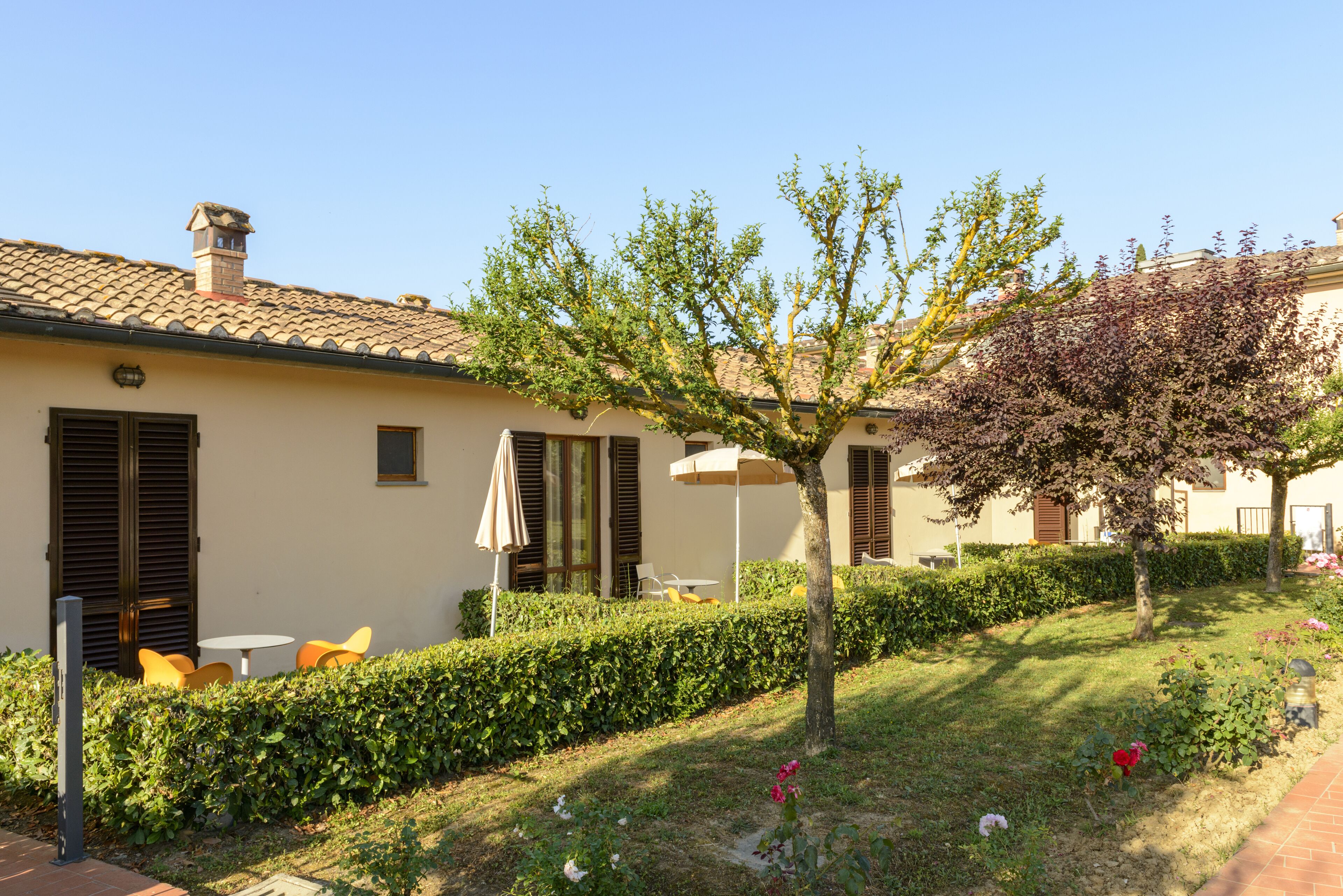 A house with a tiled roof, a garden with a tree, and outdoor seating.