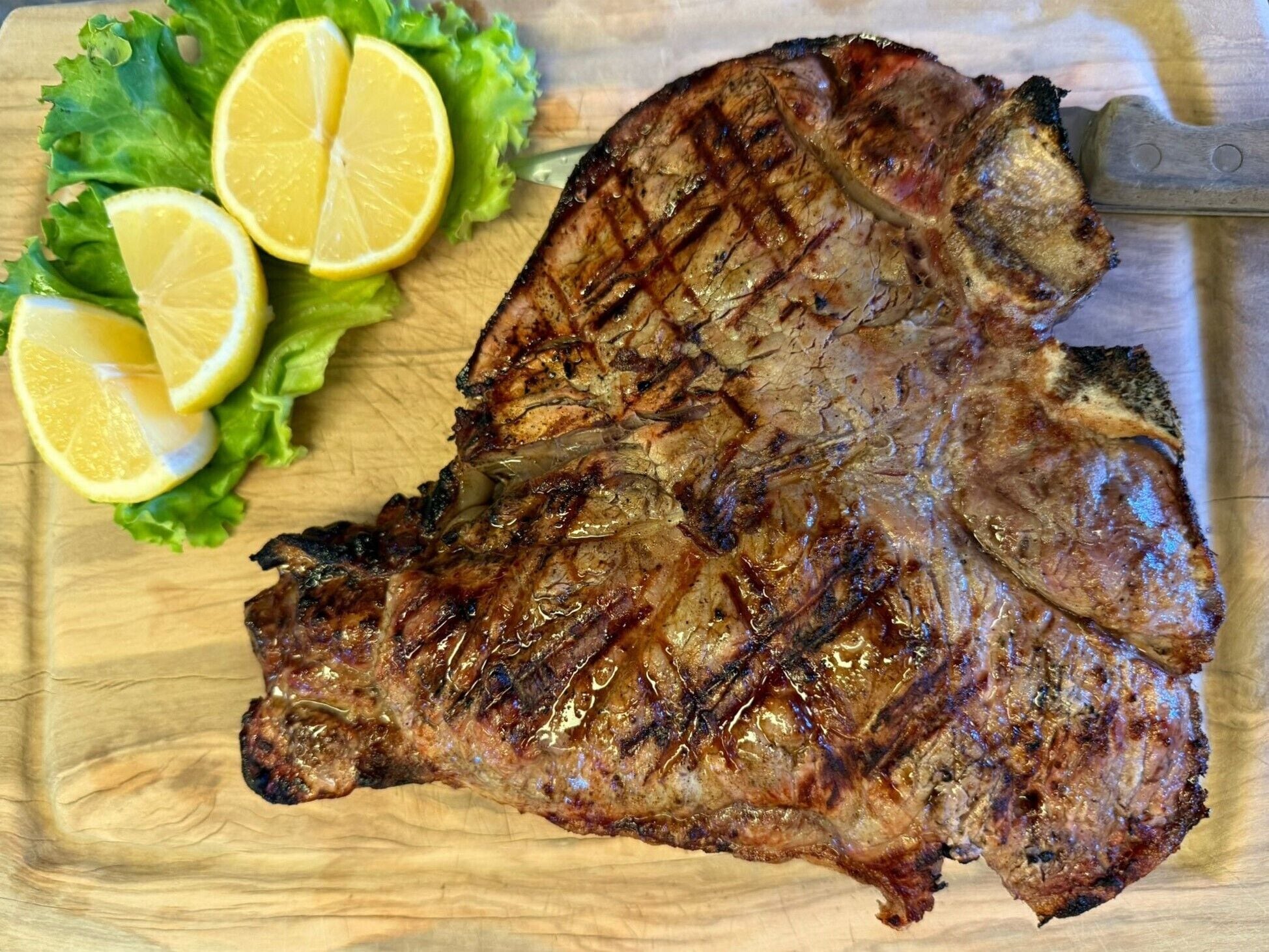Un filete a la parrilla con rodajas de limón y lechuga sobre una tabla de madera.