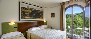 Habitación de hotel con una cama grande, una mesita de noche con un teléfono y un balcón con mesa y sillas.