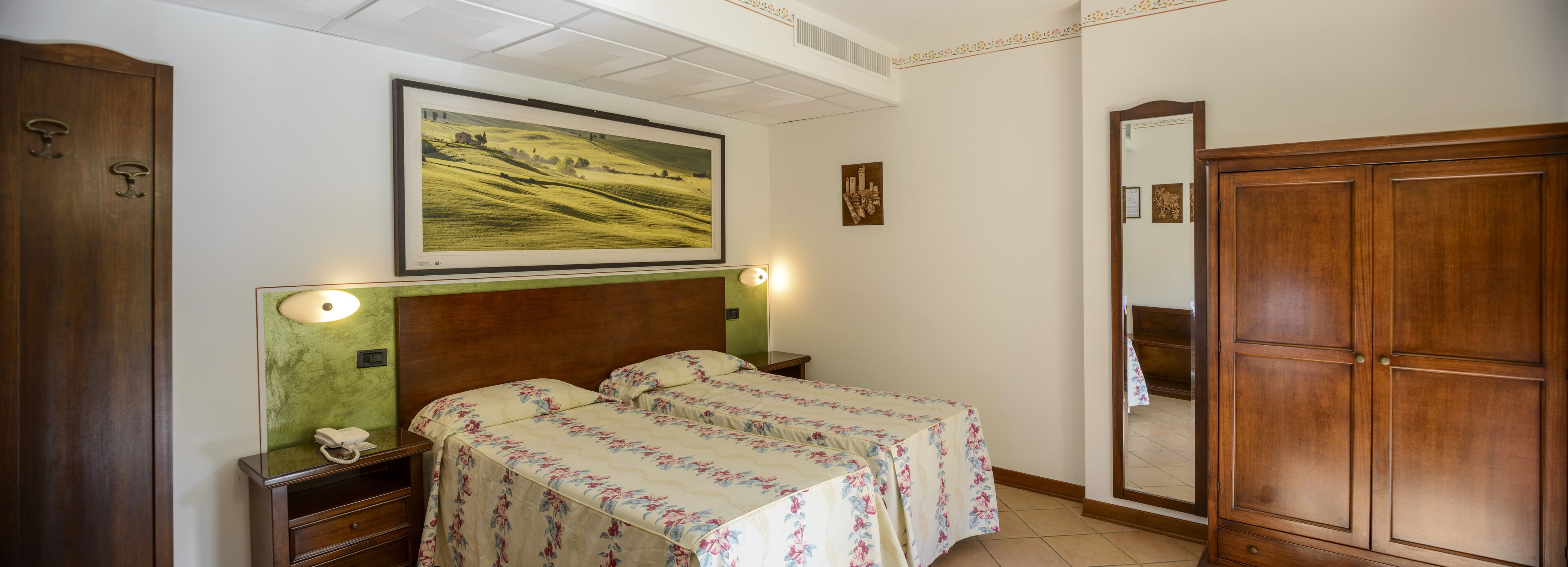 Un dormitorio con dos camas, un armario de madera, una mesita de noche con un teléfono y un cuadro enmarcado con un paisaje.