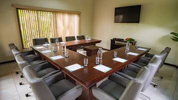 A conference room with a large table, chairs, a TV, and a window with blinds.