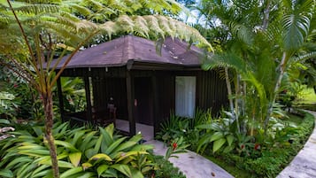 A small, dark-colored wooden structure with a roof, surrounded by lush green plants and a sign with the number 103.